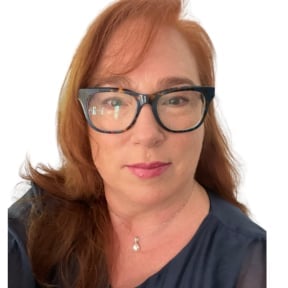 Portrait of a woman with reddish-brown hair and glasses wearing a dark blue shirt and cross necklace